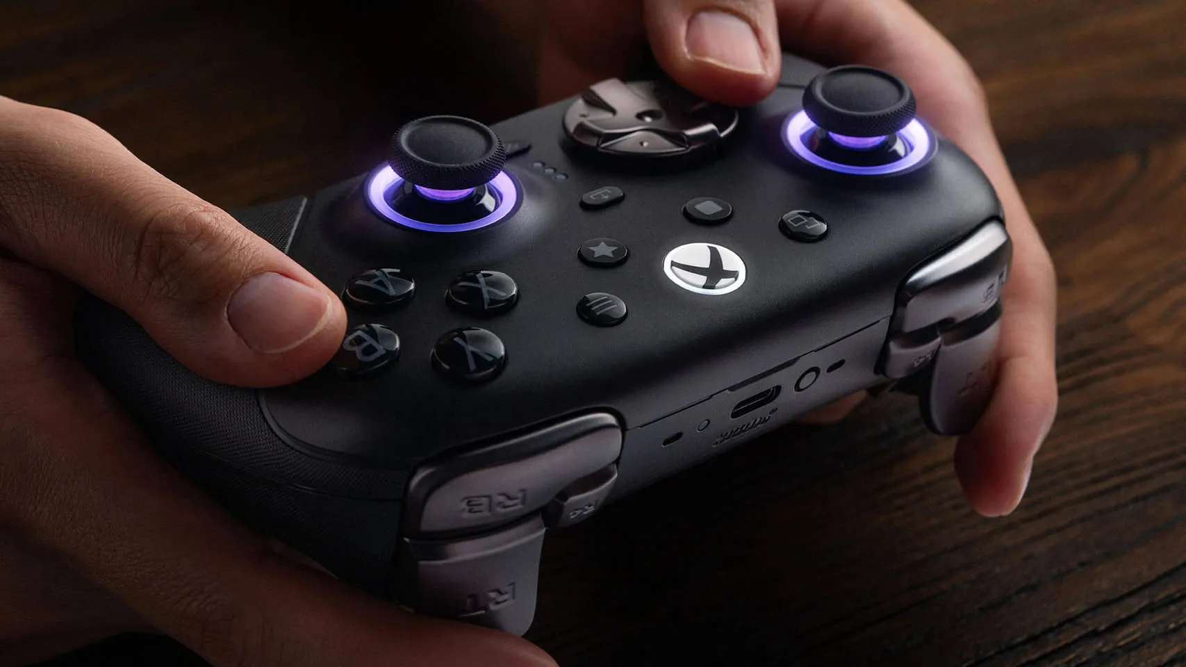 Manos sujetando el 8BitDo Ultimate 3E negro con los anillos de los joysticks iluminados en violeta